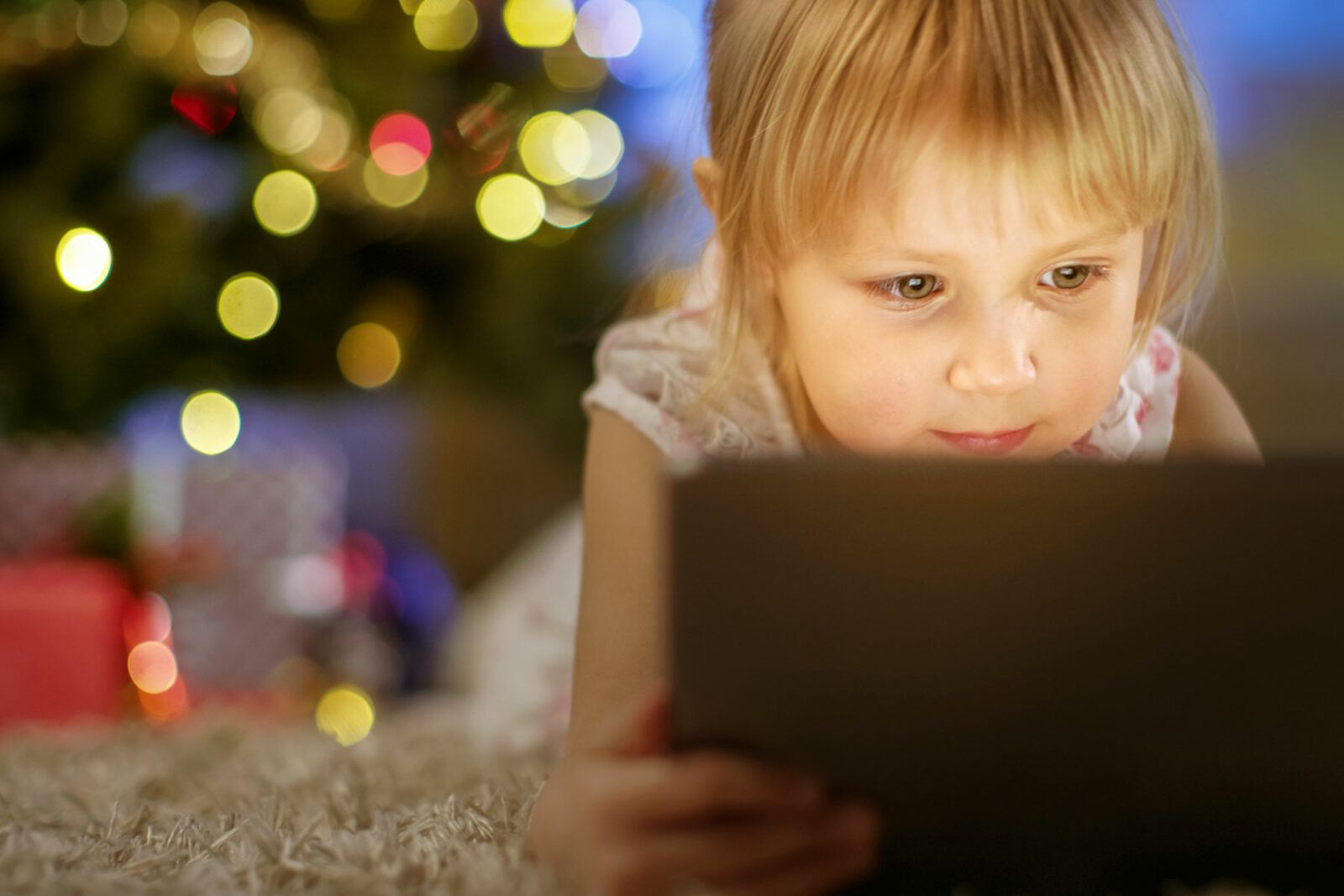 girl using tablet on clean carpeting holiday tree in background
